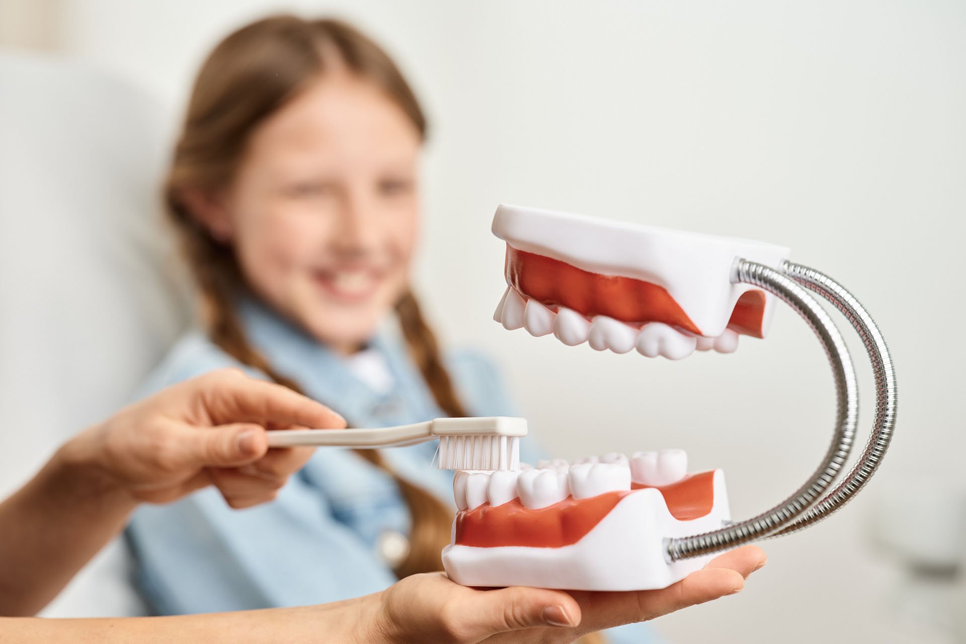 Lächelndes Mädchen lernt spielerisch die richtige Zahnpflege von ihrer KInderzahnärztin